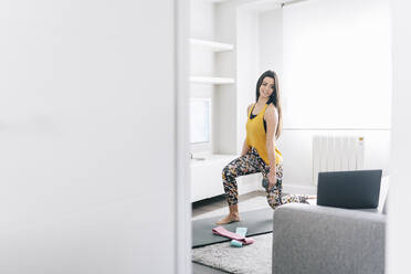 Young woman exercising with dumbbell while learning through laptop at home - DGOF02264