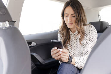 Female professional using smart phone while sitting at back seat of car - FMOF01385