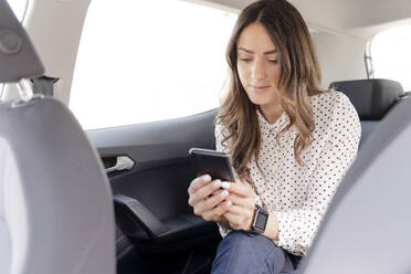 Weibliche Berufstätige, die ein Smartphone benutzen, während sie auf dem Rücksitz eines Autos sitzen - FMOF01385