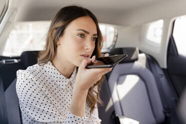 Businesswoman sending voicemail through smart phone while sitting in car - FMOF01386