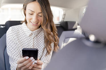 Smiling female entrepreneur using smart phone while sitting in car - FMOF01387