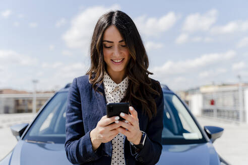 Lächelnde Geschäftsfrau mit Smartphone im Auto - FMOF01394