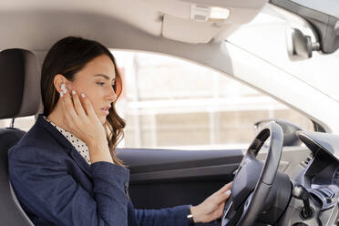 Unternehmerin spricht beim Autofahren durch In-Ear-Kopfhörer - FMOF01397