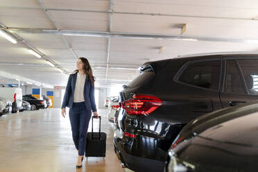 Weibliche Fachkraft geht mit Koffer auf einem Parkplatz - FMOF01403