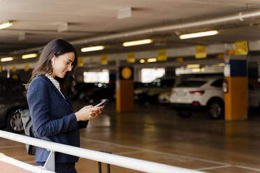 Female professional using smart phone while standing in parking lot - FMOF01407