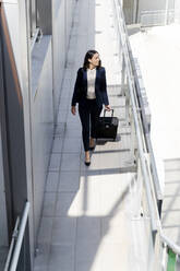 Female entrepreneur looking away while walking with suitcase in building corridor - FMOF01409