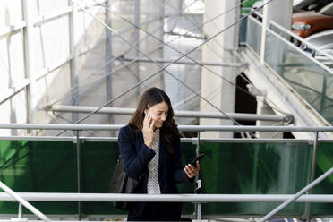 Female professional talking on smart phone while standing near railing - FMOF01411