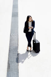 Female professional with suitcase looking away while standing outdoors - FMOF01424