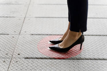 Woman standing on social distancing sticker on floor - FMOF01426