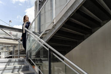 Unternehmerin schaut weg, während sie in der Nähe eines Geländers in einem Gebäude steht - FMOF01428