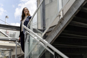 Thoughtful female professional standing near glass railing in building - FMOF01429