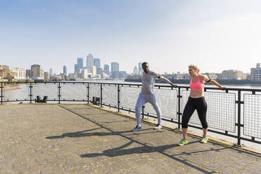 Man and woman stretching while exercising at promenade on sunny day - WPEF04577