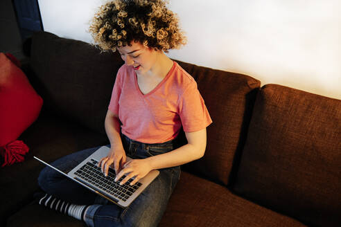 Junge Frau tippt auf dem Sofa zu Hause auf einem Laptop - ASGF00296