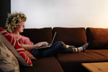 Relaxed young woman using laptop sitting on sofa at home - ASGF00297