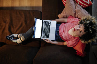 Schöne Frau mit Laptop sitzt auf Sofa im Wohnzimmer - ASGF00300