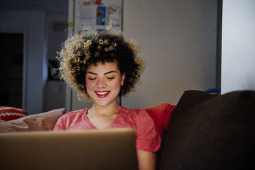 Smiling beautiful woman using laptop in living room at home - ASGF00305