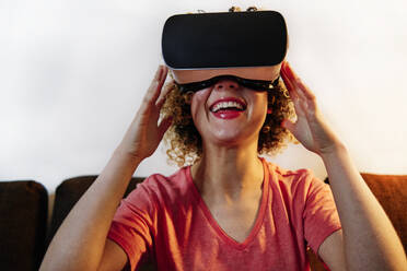 Cheerful young woman wearing virtual reality simulator in living room - ASGF00307