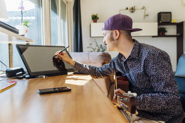 Junger männlicher Komponist mit Gitarre und Grafiktablett zu Hause - MEUF03020