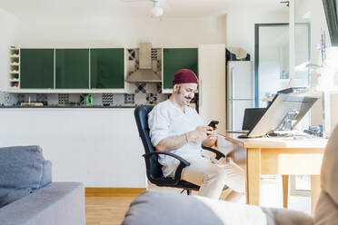 Smiling young man using mobile phone at home - MEUF03044