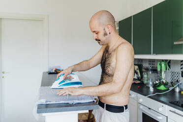 Hemdenloser Mann bügelt Hemd auf Kücheninsel zu Hause - MEUF03046