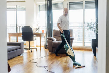 Mann mit Schnurrbart reinigt Boden mit Staubsauger zu Hause - MEUF03047