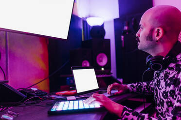 Male composer looking at device screen while composing music at home studio - MEUF03077