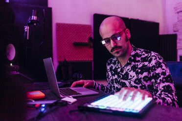 Male composer wearing eyeglasses touching digital tablet while composing music at studio - MEUF03083