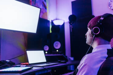 Mann mit Strickmütze schaut auf den Bildschirm eines Geräts, während er im Studio Musik hört - MEUF03094