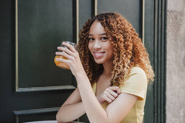 Young woman holding orange juice glass outdoors - EBBF03677