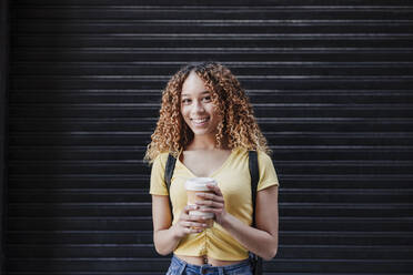 Young woman with reusable cup standing in front of black shutter - EBBF03702