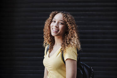 Young woman smiling in front of black shutter - EBBF03704