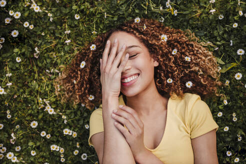 Young woman wearing flowers while lying on meadow - EBBF03716