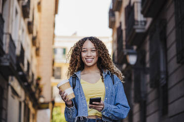 Young woman with mobile phone and reusable cup in city - EBBF03719