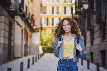 Smiling woman in denim clothing standing in alley near buildings - EBBF03721