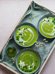 Top view of delicious pea cream soup in bowls served on table with napkin and vase with flowers - ADSF24598