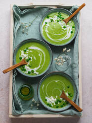 Top view of delicious pea cream soup in bowls served on table with napkin and vase with flowers - ADSF24599