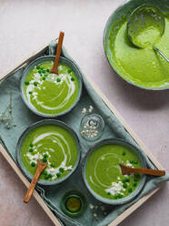 Top view of delicious pea cream soup in bowls served on table with napkin and vase with flowers - ADSF24600