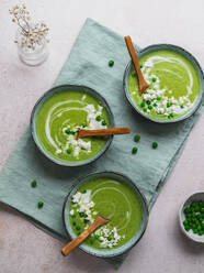 Draufsicht auf eine köstliche Erbsencremesuppe in Schalen, serviert auf einem Tisch mit Serviette und Vase mit Blumen - ADSF24602