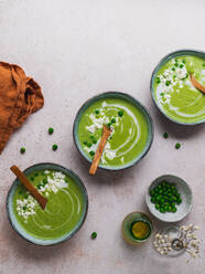 Top view of delicious pea cream soup in bowls served on table with napkin and vase with flowers - ADSF24603