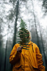 Erwachsener weiblicher Reisender mit üppigem grünen Pflanzenblatt, der während eines Ausflugs im Wald wegschaut - ADSF24621