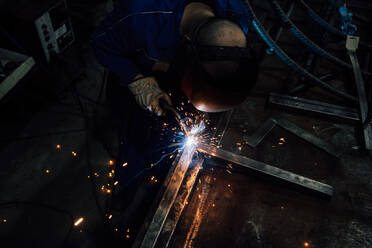 Crop gesichtslosen Arbeiter in Handschuhen und Uniform Schweißen Metallteile auf dem Tisch in der Nähe von Konstruktionen in der Fabrik - ADSF24630