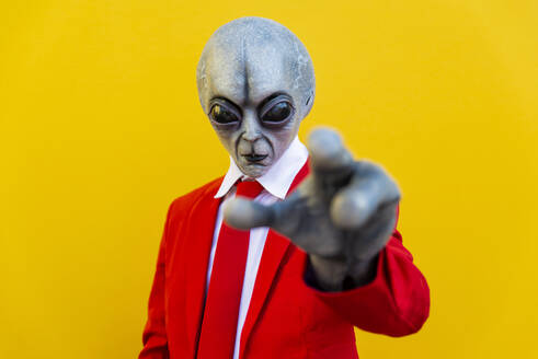 Portrait of man wearing alien costume and bright red suit reaching toward camera - OIPF00682