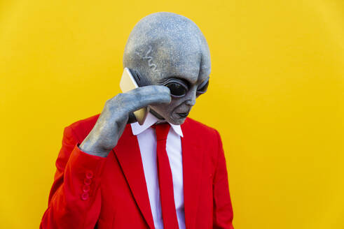 Portrait of man wearing alien costume and bright red suit using smart phone - OIPF00684