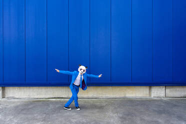 Mann in leuchtend blauem Anzug und Panda-Maske steht mit erhobenen Armen im Freien - OIPF00694