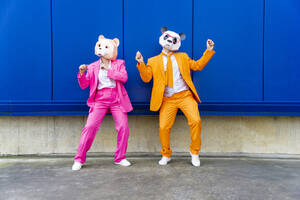 Mann und Frau in farbenfrohen Anzügen und Bärenmasken tanzen Seite an Seite gegen eine blaue Wand - OIPF00701