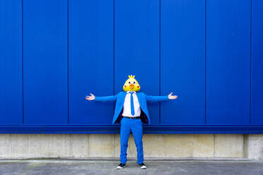 Mann in leuchtend blauem Anzug und Vogelmaske steht mit offenen Armen im Freien - OIPF00719