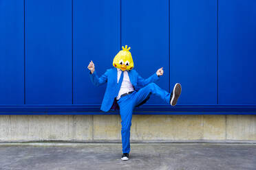 Mann in leuchtend blauem Anzug und Vogelmaske steht auf einem Bein vor einer blauen Wand - OIPF00721