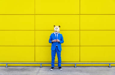 Mann in leuchtend blauem Anzug und Nagetiermaske vor einer gelben Wand - OIPF00736