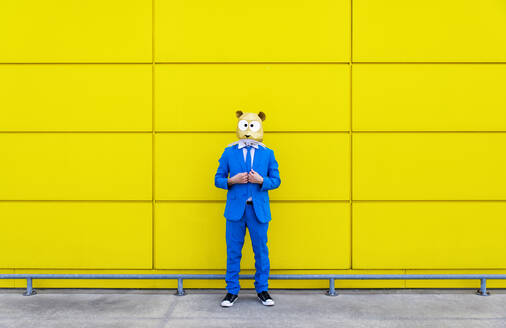 Mann in leuchtend blauem Anzug und Nagetiermaske vor einer gelben Wand - OIPF00736