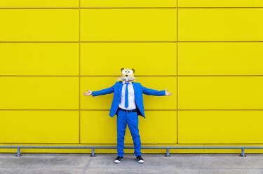 Mann in leuchtend blauem Anzug und Nagetiermaske steht mit ausgestreckten Armen vor einer gelben Wand - OIPF00739